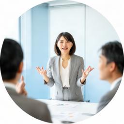 明るい研修室で話し方を指導する日本人女性講師、受講者に身振りで説明する様子